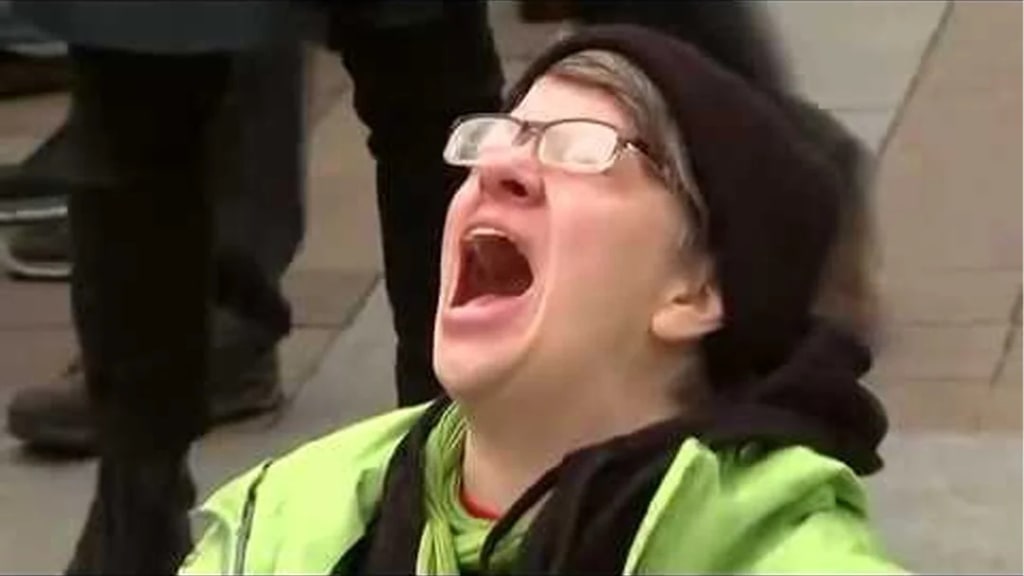 A person wearing glasses and a green jacket shouts with their mouth open.